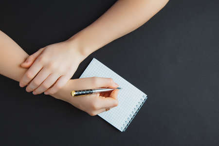 A female hands hold a book spread on the wooden desk with pen, top view at the studio.