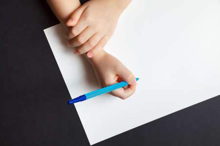 Child's hands over empty white the sheet of paper blue pen on the dark background. Concept of a...