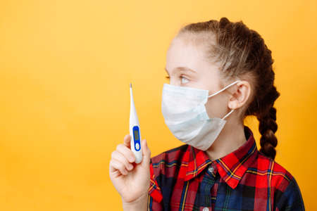 A Teenage girl on a Yellow Background Holds a Thermometer in her hand and Looks Away.