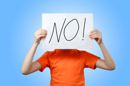 Teen girl on a blue background holding a piece of paper with the word No in front of herの写真素材
