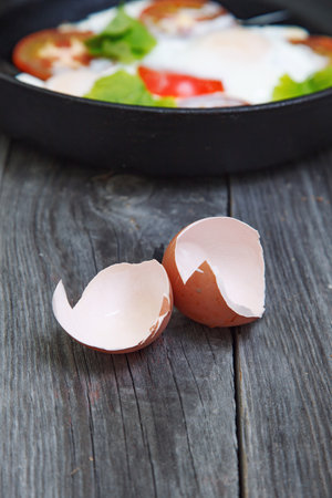 Eggshell and Omelette with tomato and greens on cast iron frying pan. Rustic breakfast omelette with...