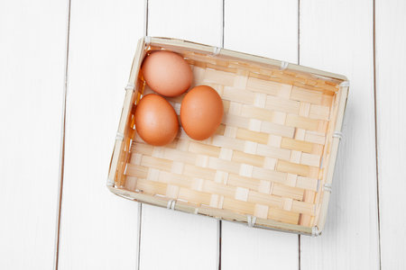 Three brown eggs in basket on a wooden background.の写真素材