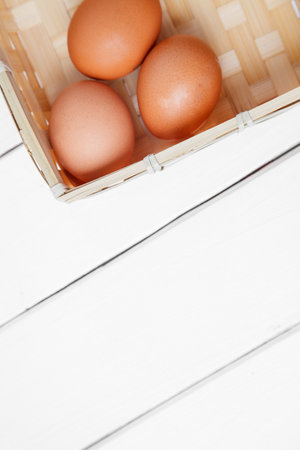 Three brown eggs in basket on a wooden background. top view. vertical shoot