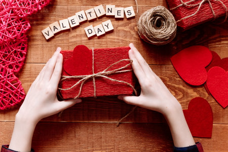 Hearts, gift, ribbons, envepopes on wood background. Girls hands making handmade valentines day decorationの写真素材