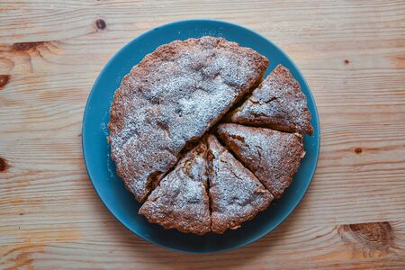top view homemade cake sprinkled with icing sugar on a plate on a wooden table.の写真素材