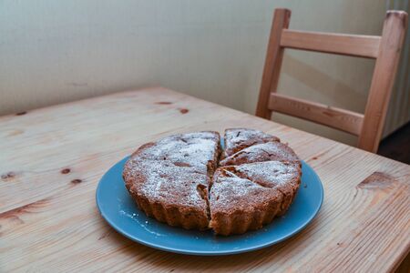 homemade cake sprinkled with icing sugar on a plate on a wooden table.