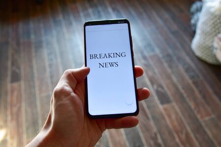 close up man's hand holding mobile phone device with news feed.の写真素材