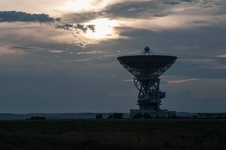 Space radar antenna. Satellite dish at sunset with cloudy sky.の写真素材