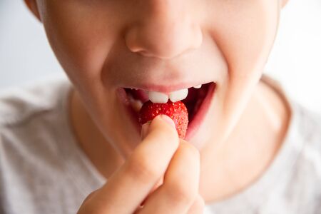 boy eating a very tasty strawberry on a light background. Close up.の写真素材