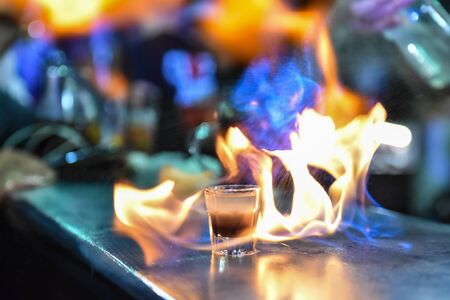 Glass with an alcoholic drink on fire at a bar counter. Fiery show at the bar. The bartender makes hot alcoholic cocktail and ignites bar. Fire on bar.の写真素材