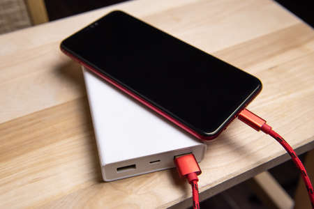 Smartphone charging with power bank on wood board.