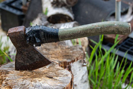 An old rusty ax with a wooden handle is rewound with a black ribbon, stuck in a birch stump against...