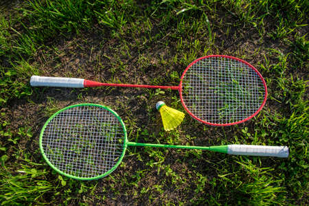 Two badminton rackets with a yellow shuttlecock on the green grass, summer active games.