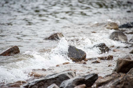 small stones on the seashore, the rolling waves of the sea with foam.の写真素材