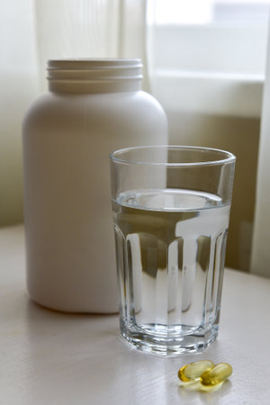 Omega-3, spirulina, chlorophyll capsules and glass of water on white wooden table. Dietary supplements, biologically active additives. vitamin pills. Health support.の写真素材