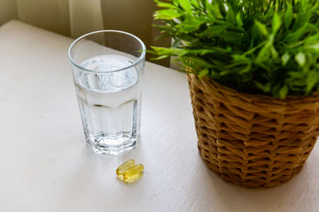 Omega-3, spirulina, chlorophyll capsules and glass of water on white wooden table. Dietary supplements, biologically active additives. vitamin pills. Health support.の写真素材