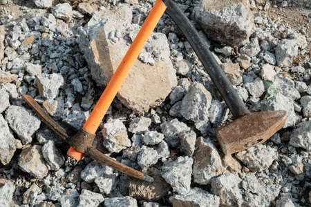 Geological pick with orange handle on the stones next to old hammer.