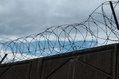 Stone wall with barbed wire against blue sky.の写真素材