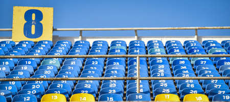 Tribune of fans at the stadium. Lots of rows with blue and yellow seats for people on the football field.の写真素材