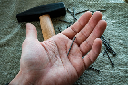 metal nails in a man's hand. in the background a hammer and a bunch of nails.の写真素材
