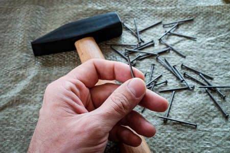 metal nails in a man's hand. in the background a hammer and a bunch of nails.