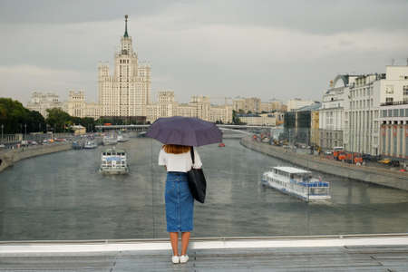 a girl under an umbrella stands on the bridge and looks at the ships sailing along the river.の写真素材