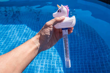Checking the temperature of the swimming pool water with a funny thermometer. Unicorn pool thermometer.の写真素材