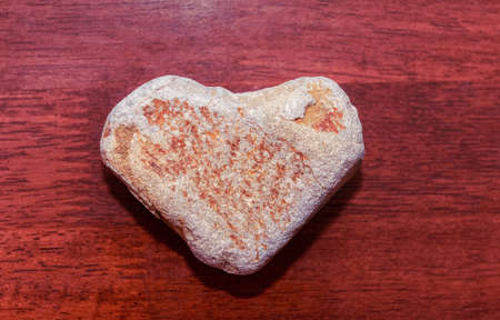 stone shaped like a heart on a wooden surface in red tone. Heart made of natural stone on a wooden background. Valentine's day and holiday concept.の写真素材