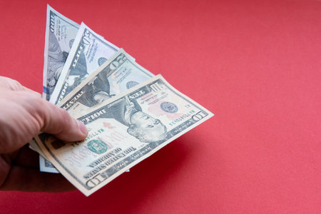 Mans hand hold dollar banknotes of different denominations Close up on red background.の写真素材