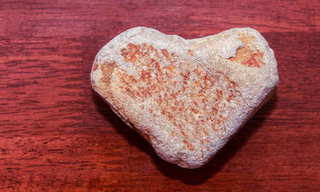 stone shaped like a heart on a wooden surface in red tone. Heart made of natural stone on a wooden background. Valentine's day and holiday concept.の写真素材
