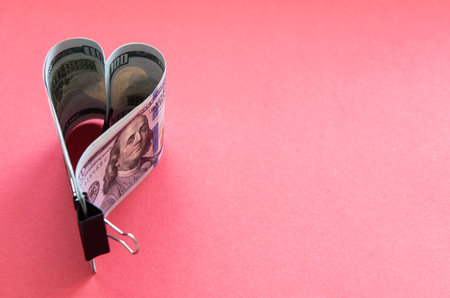 Heart made of dollar bills on a red background.の写真素材