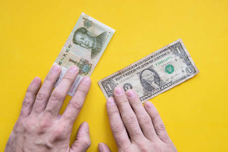male hands from above on the dollar and yuan banknotes on a yellow background. USA money and china money. US dollar vs Chinese yuan CNY.の写真素材