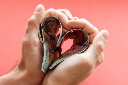several 100 dollar bills folded in the shape of a heart in male hands. love of money, greed,...