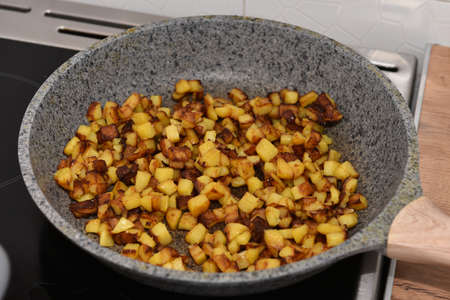 delicious crispy golden fried potato cubes on an old metal frying pan close-up. Cooking homemade fried potatoes in a pan.の写真素材