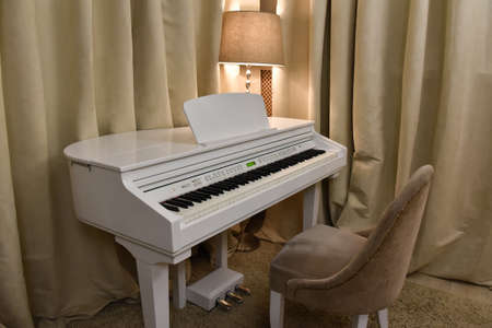 white piano with a chair standing in a room with a floor lamp and curtains.の写真素材