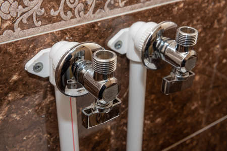 Water taps for connecting a boiler on tiled wall. The faucet with connected pipes is mounted on the...