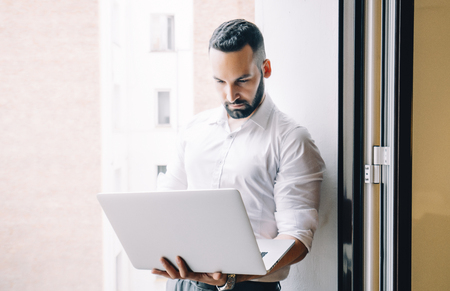 Attractive man with a beard working with a computer and mobile phone on the terrace of the house.の写真素材