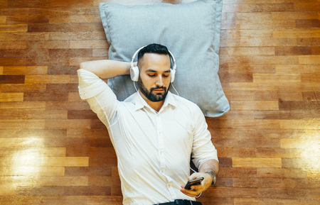 Attractive man and beard listening to music lying on floor of house.の写真素材