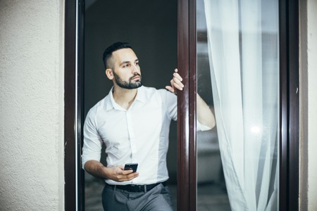 Attractive man with beard working posing at home window.の写真素材