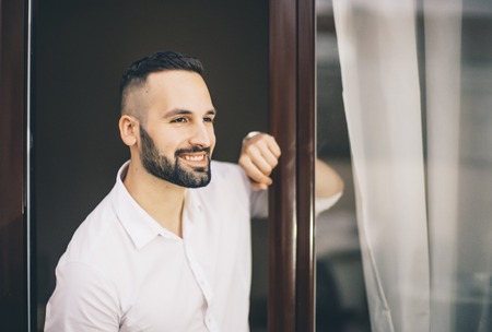 Attractive man with beard posing to camera in the window of the house.の写真素材