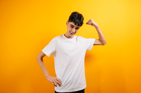 Teen boy flexing arm, confident, yellow background.の写真素材