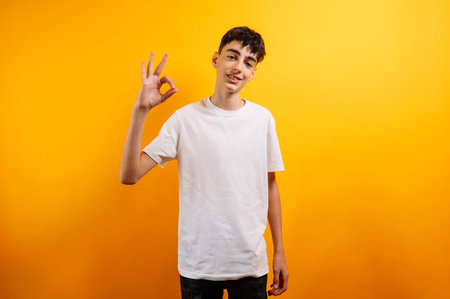 Teen boy smiles, makes okay hand gesture, yellow background.の写真素材