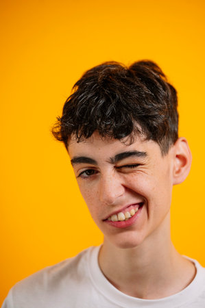 Teen boy winks playfully against yellow background.