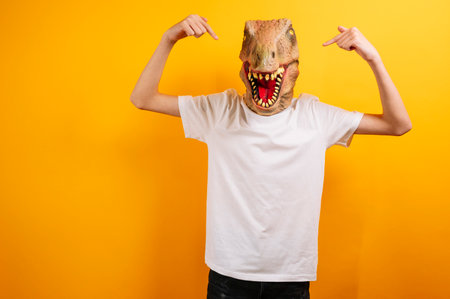 Teenager with T-Rex mask on yellow backgroundの写真素材