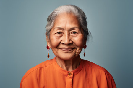 Smiling elder Inuit woman in casual wear, posing against a blue studio backgroundの素材