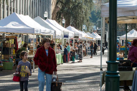 Many people at Portland farmer's market in Oregon on a sunny day. People can be seen laughing standing listening looking walking and smiling. Local business owners offering samples answering questions and making sales to customers from their tents or kiosのeditorial素材