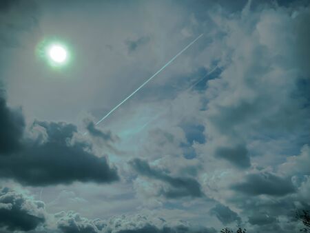 Plane contrails on a dramatic cloudy sky with bright sun in the sky.