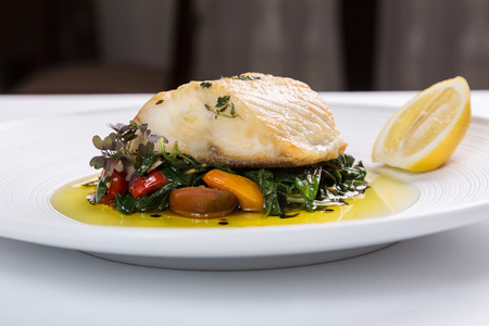 Fish filet served with grilled vegetables on a white plateの写真素材