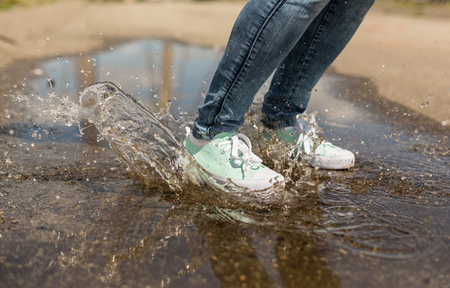 Woman in gumshoes jumping in a puddle. Close up shot of foots in a shoes with water splashesの写真素材