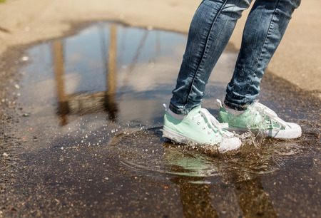 Woman in gumshoes jumping in a puddle. Close up shot of foots in a shoes with water splashesの写真素材